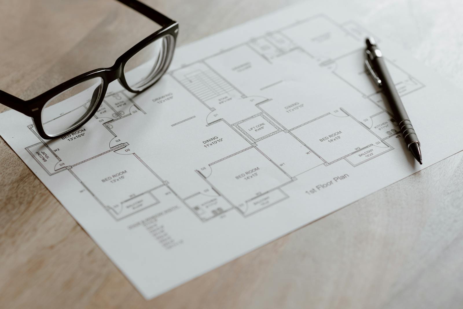 A close-up of a floor plan with eyeglasses and a pen on a wooden table, ideal for architecture projects.