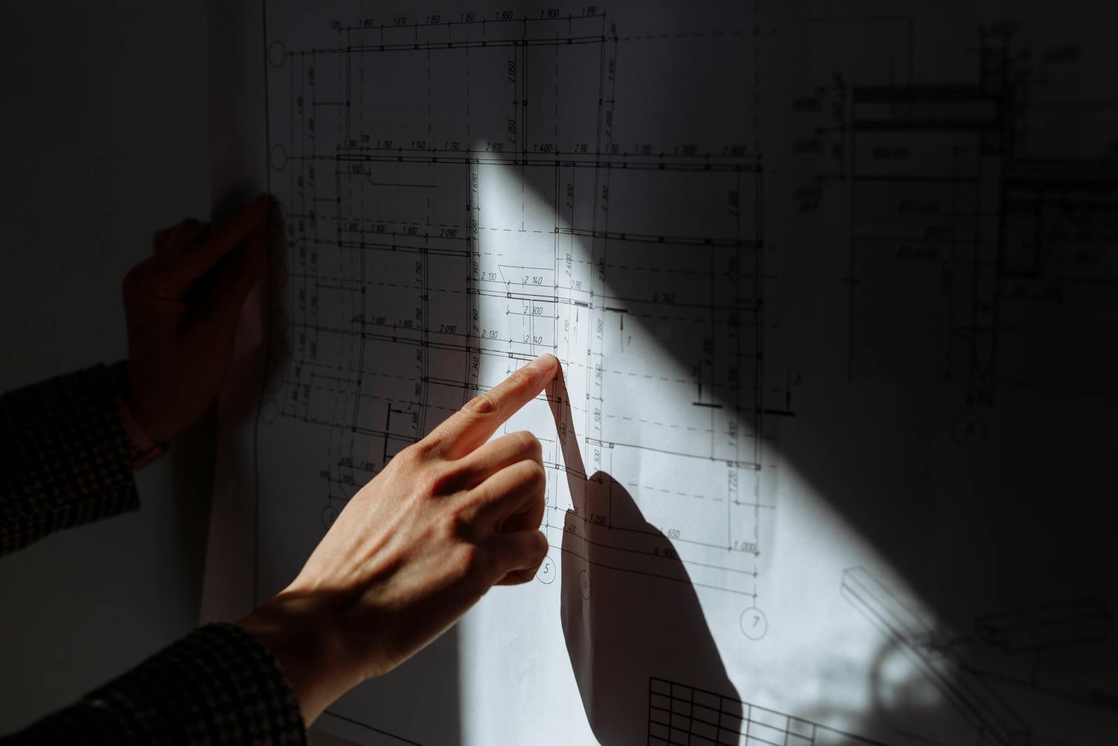 A detailed examination of construction blueprints under dramatic lighting.